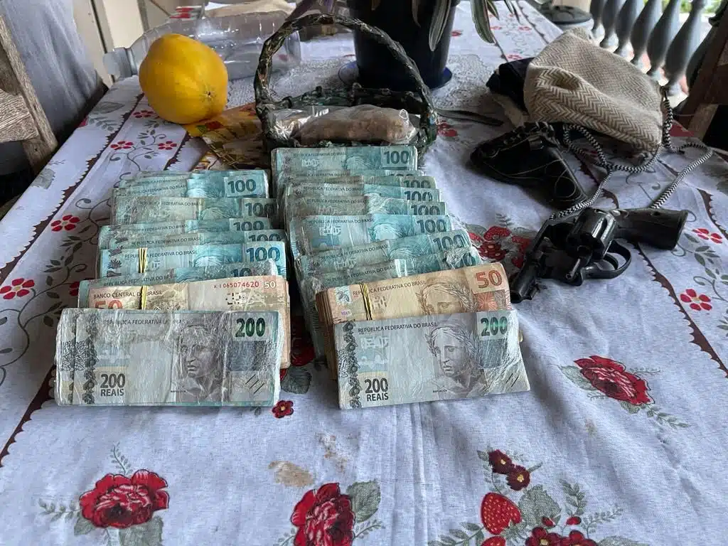 Imagem com maços de dinheiro em cima de uma mesa forrada com toalha branca e flores vermelhas