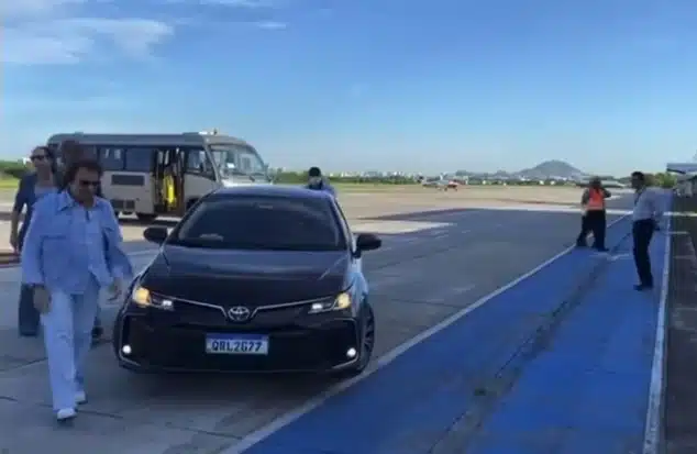 Roberto Carlos, de roupas claras e óculos escuros, saindo de um veículo e caminhando no aeroporto