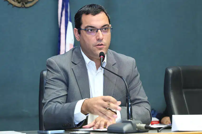 De frente para o observador. Homem de terno, com óculos , falando ao microfone