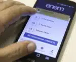 Enem abre inscrições: saiba mais sobre o cronograma mão tocando em um smartphone para inscrição no enem