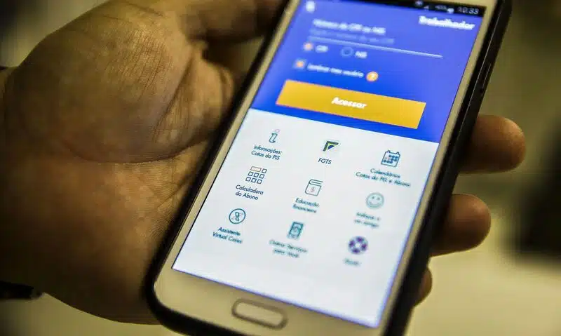 Celular com a tela inicial do aplicativo FGTS aberta. O celular está na mão de uma pessoa.