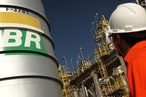 Homem usano uma blusa vermelha e capacete branco, olha para um tanque com a logo da Petrobras
