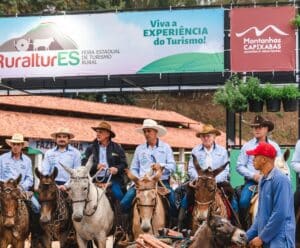 15ª Expedição Tropeira: Rota da Imigração recria a jornada dos italianos no ES Varias pessoas estão montadas em cavalos, de baixo de uma faixa que apresenta a partida da expedição.