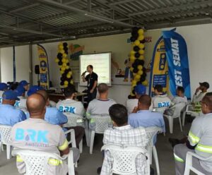 BRK destaca atitudes seguras no trânsito no Maio Amarelo Na imagem, várias pessoas estão sentadas pelaem cadeiras de plastico e estão de costas, olhando para o palestrante que explica sobre segurança no trânsito.