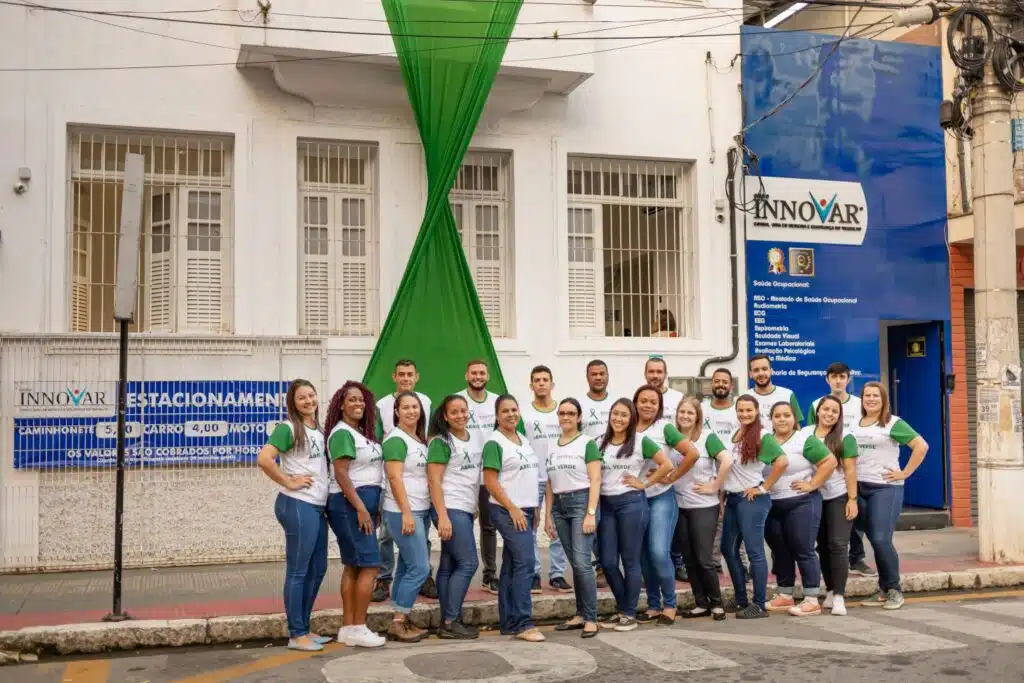 Um grupo de funcionários posam para a foto em frente da fachada do grupo. 