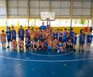 Crianças com o uniforme da Lusb, possam para foto com seus treinadores em uma quadra.