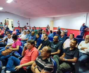 Varias pessoas estão sentadas em um auditório, escutando atentamente o que está sendo dito na palestra.