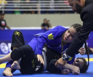 A atleta Stephanie Balista esta sob a adversaria em uma quadra dando uma finalização na oponente.