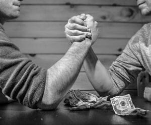 Valores Duas pessoas estão em uma queda de braço, enquanto um bolo de dinheiro esta na frente deles.
