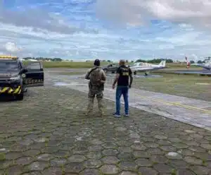 Avião de igreja é flagrado com 290 quilos de maconha; PF é acionada Dois policiais ao lado da viatura observam o avião da igreja com maconha