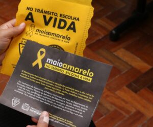 mão de homem segurando propaganda do Maio Amarelo