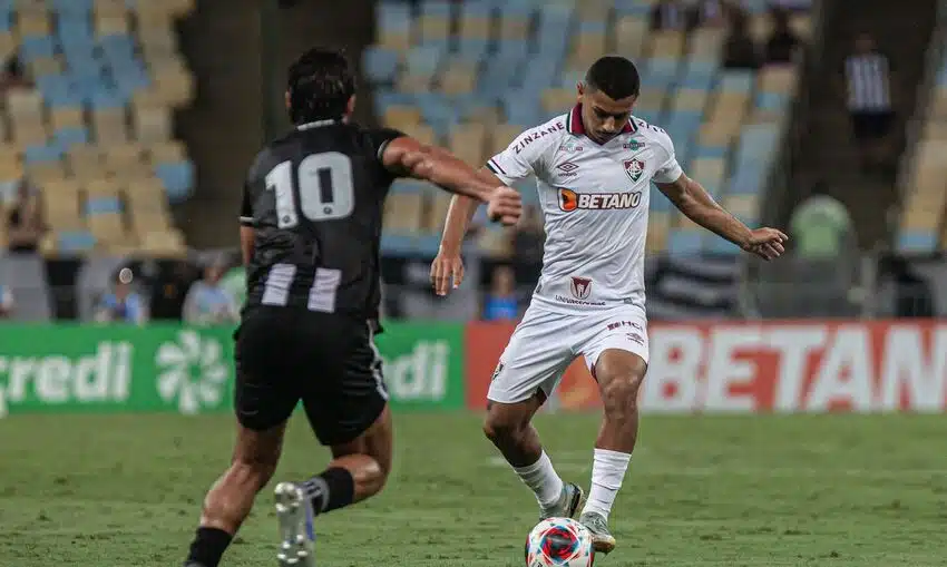 Jogador do Fluminense com a bola nos pés se livrando do marcador do Botafogo