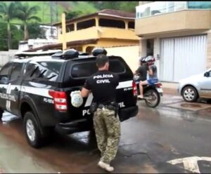 Homem com camisa da Polícia Civil fechando o porta-malas de uma viatura