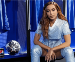 Anitta agita público com funk brasileiro na final da Champions League Annita ao lado de uma bola de futebol dentro de um vestiário