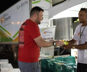 Shows da Festa de Cachoeiro terão entrada solidária Rapaz entregando alimentos a outro rapaz