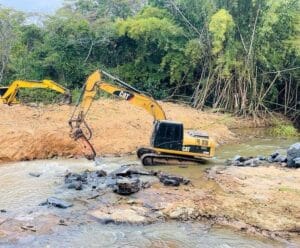 Foto mostra máquina dentro do Rio Calçado fazendo a retirada de uma pedra para evitar enchentes