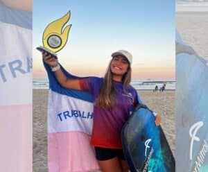 Atleta segura um troféu e uma prancha na praia