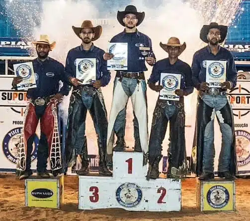 Foto mostra peão campeão do rodeio de Muniz Freire no pódio com outros competidores