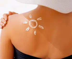 A sua pele precisa de cuidados essenciais no verão; aprenda quais mulher de costas com filtro solar desenhado um sol