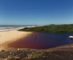 Praia do ES faz divisa com lagoa de cor avermelhada. Conheça
