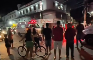 Pessoas observam a movimentação de socorro após um acidente à noite em Marataízes. Uma ambulância do SAMU está estacionada com as luzes de emergência ligadas em frente a um hotel na avenida Simão Soares, enquanto moradores acompanham a cena na rua.