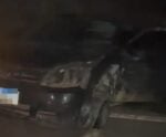 Carro preto com a frente danificada após acidente à noite na BR-262, próximo a Ibatiba, Espírito Santo. O veículo está parado no acostamento com sinais de colisão e roda dianteira comprometida. Faróis parcialmente acesos.