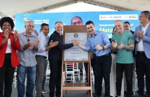 Minha Casa, Minha Vida: mais de 900 unidades são entregues em Linhares Autoridades e representantes celebram a inauguração do Residencial Mata do Cacau, do programa Minha Casa, Minha Vida, em Linhares (ES). Ao centro, duas autoridades apertam as mãos diante de uma placa comemorativa, cercadas por outras pessoas aplaudindo, sob uma tenda com painel ao fundo exibindo informações do evento.