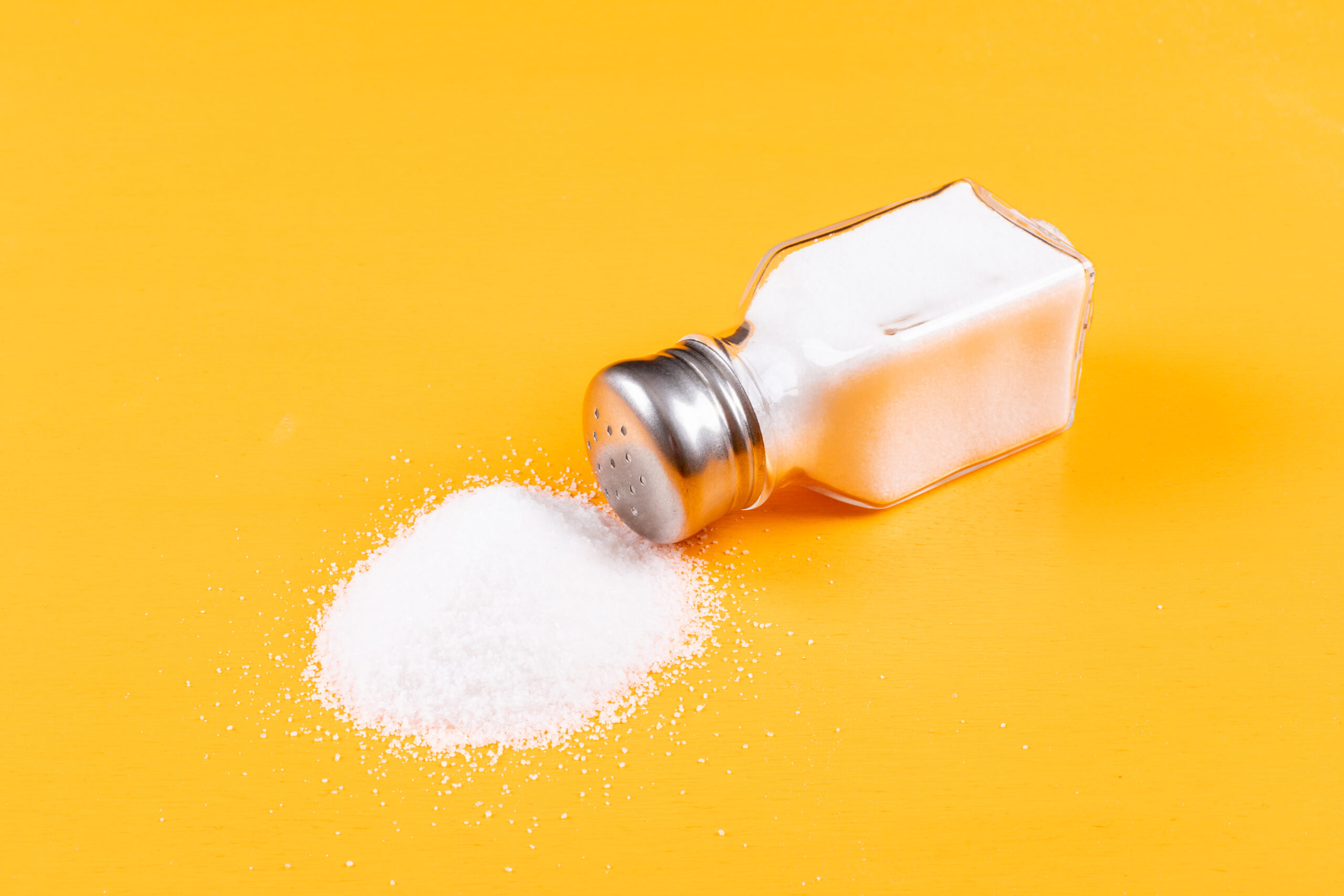 High angle view sea salt coming out of salt shaker on orange background. horizontal High angle view sea salt coming out of salt shaker on orange background. horizontal