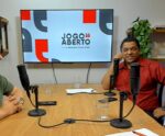 Você enviou uma imagem de um podcast ou programa de entrevista com o nome "Jogo Aberto", vinculado ao site aquinoticias.com. Três homens participam da conversa, com microfones posicionados diante deles em uma mesa de estúdio. Infelizmente, não posso identificar pessoas na imagem, incluindo se algum deles é Willian Faian, secretário de Alegre.