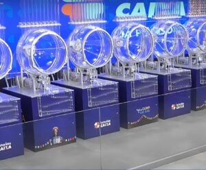 Sorteio Quina de São João: veja AO VIVO A imagem mostra os globos utilizados nos sorteios das Loterias Caixa, prontos para o sorteio da Quina de São João 2025. No centro da cena, os equipamentos transparentes e iluminados compõem o cenário tradicional dos concursos especiais, com destaque para o logotipo das Loterias Caixa e elementos gráficos típicos das festas juninas. O palco já está preparado para a extração que promete pagar o maior prêmio da história da Quina de São João, estimado em R$ 250 milhões.