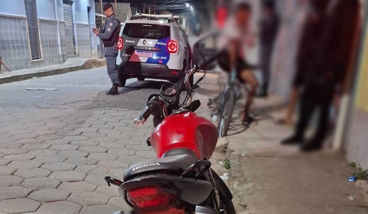 Imagem ilustra policial ao fundo ao lado de uma viatura. Em primeiro plao uma motocicleta vermelha