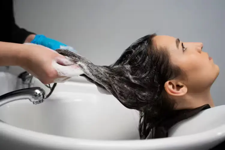 Mulher lavando o cabelo em salão de beleza com shampoo espumante, recebendo cuidados capilares profissionais como parte de uma rotina de cronograma capilar.