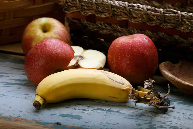 Banana e maçãs sobre uma mesa rústica, representando alimentos naturais com calorias nutritivas e saudáveis para a dieta.