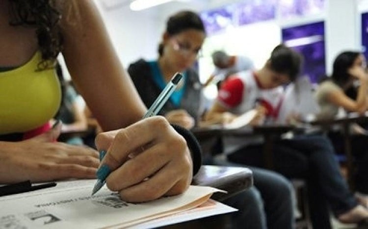 Candidatos realizam a prova nacional docente em sala de aula, concentrados e escrevendo em folhas oficiais do exame.