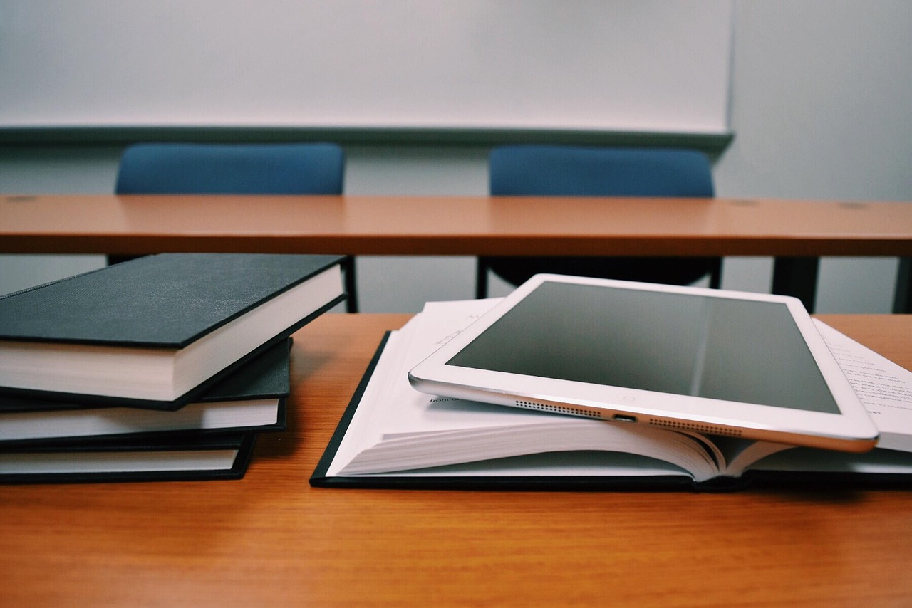 Livros empilhados e um tablet sobre a mesa de uma sala de aula, simbolizando conhecimento, tecnologia e a valorização dos professores no contexto do projeto de isenção do Imposto de Renda.