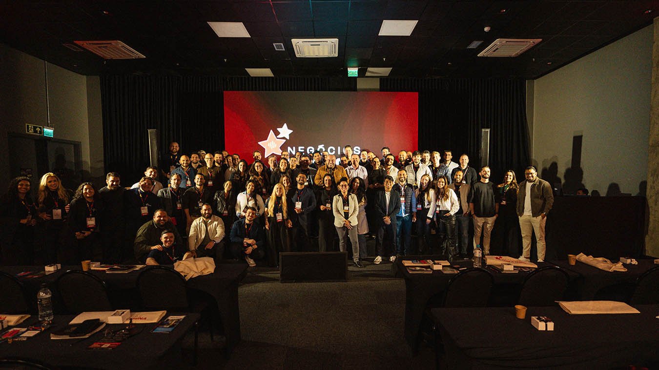 Grupo de empresários reunidos no evento Negócios com a China, durante imersão sobre importação e comércio internacional, realizado em auditório com telão de fundo vermelho e logo do evento projetado, simbolizando networking e aprendizado empresarial em Vitória, Espírito Santo.