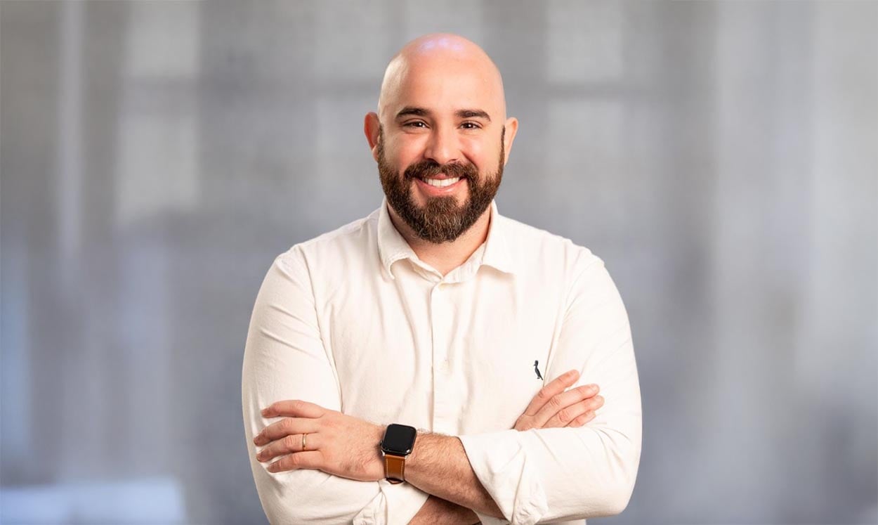 Profissional da área de engenharia posando para foto institucional, com camisa social clara, braços cruzados e expressão sorridente, representando atuação em perícias, auditorias, projetos e consultorias em engenharia civil e ambiental.