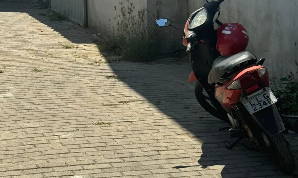 Moto Honda Biz estacionada em uma rua com um capacete em cima do banco.