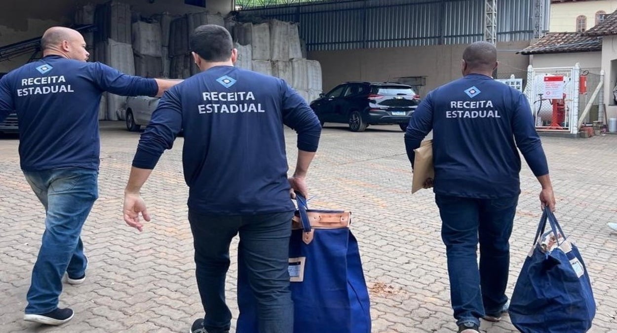 Agentes da Receita Estadual caminham com sacolas apreendidas durante operação contra fraude no comércio de café.