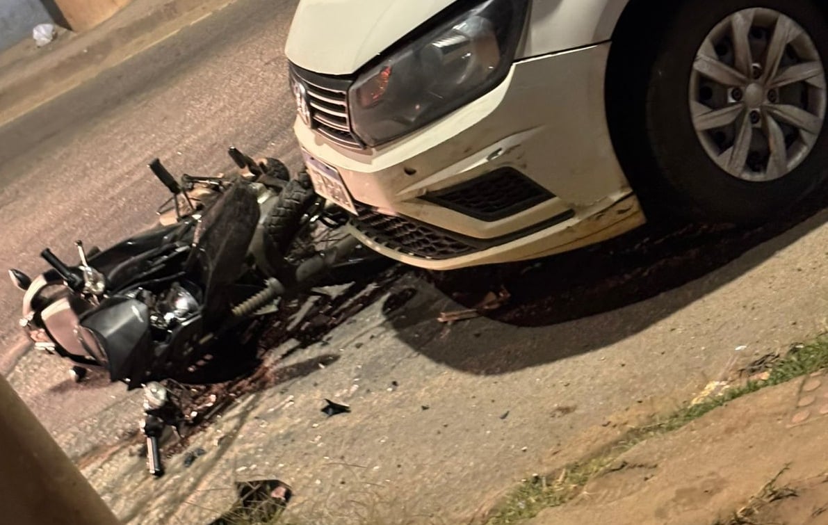 Carro branco com para-brisa quebrado e frente danificada após colisão com motocicleta caída ao lado, na Avenida Mauro Miranda Madureira, em Cachoeiro de Itapemirim.