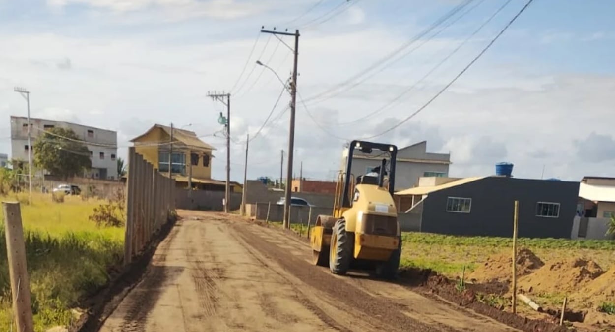 Máquina compactadora trabalha em uma rua de terra em Marataízes, mostrando uma via cheia de obras e melhorias na comunidade da Praia dos Cações.