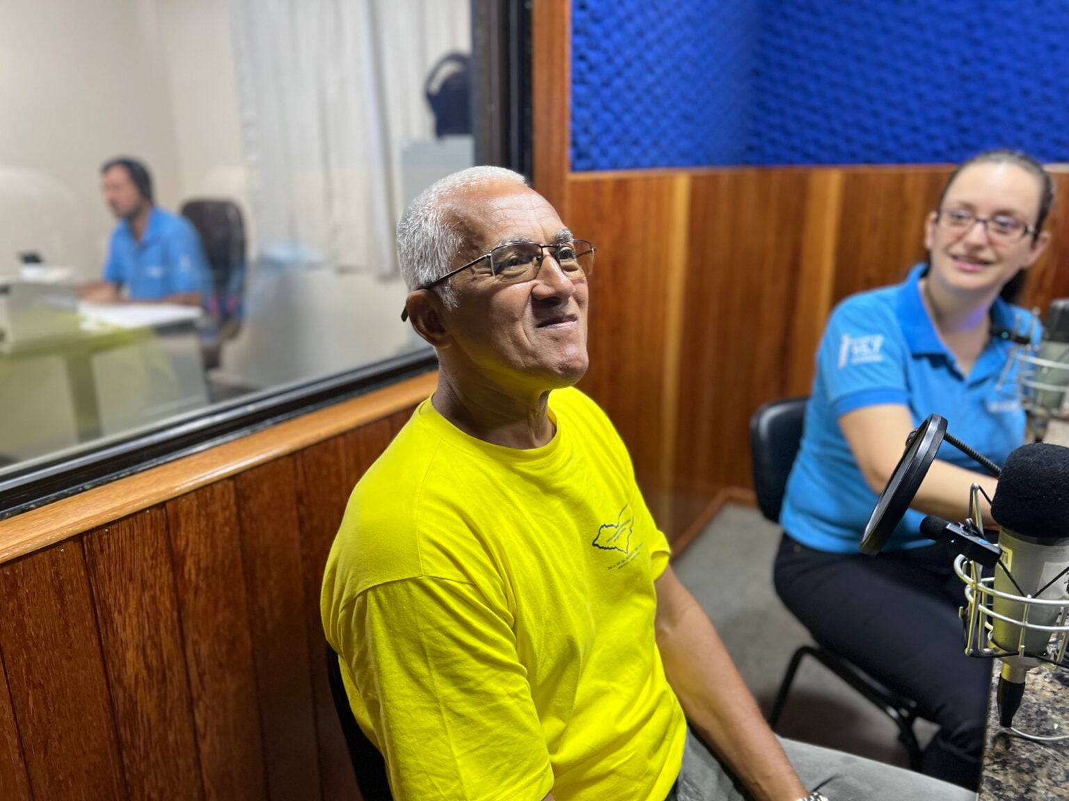 Imagem retrata homem de camisa amarela participando de programa de rádio