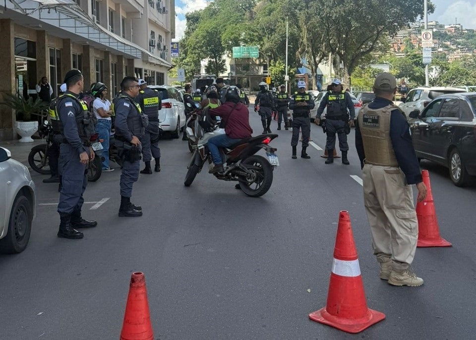 Imagem retrata blitz, com policiais abordando motociclistas.