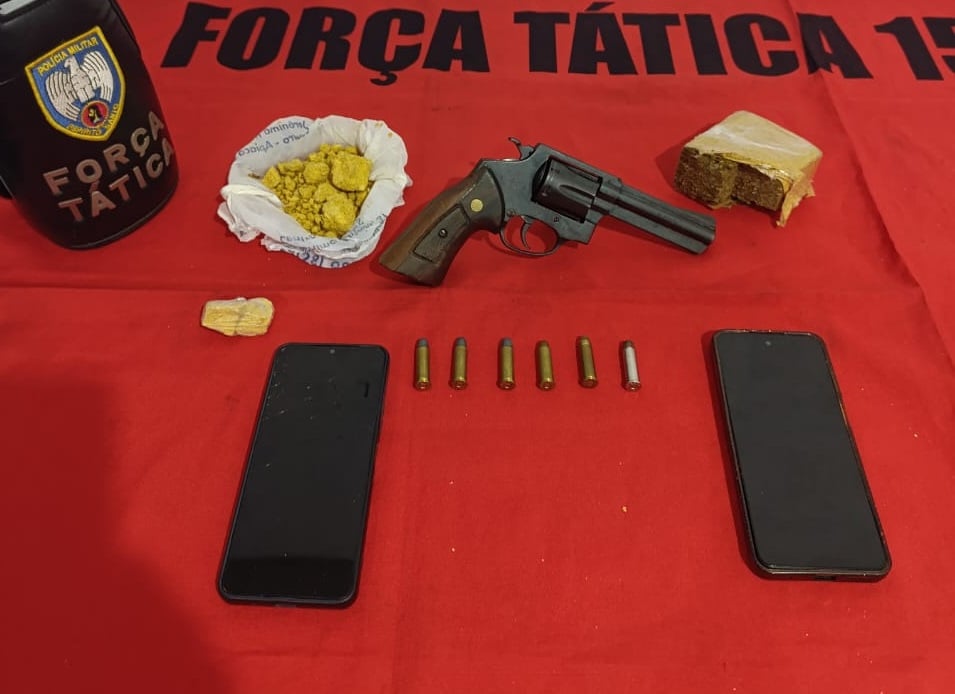 Pano vermelho sobre a mesa, com nome da Polícia Militar, celulares roubados, drogas e arma sobre a mesa.