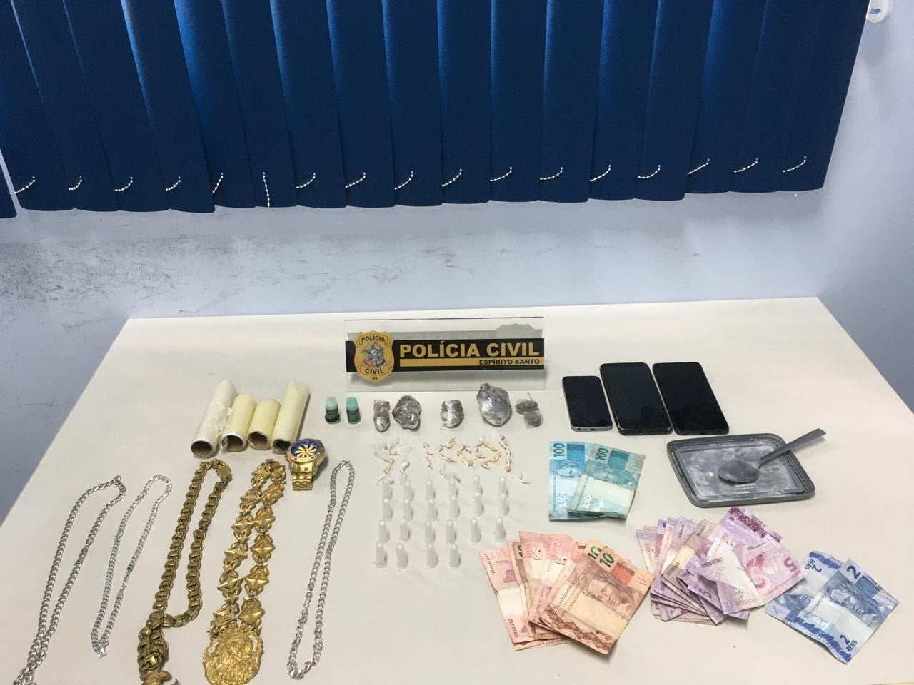 Imagem retrata drogas e objetos roubados em cima de uma mesa.