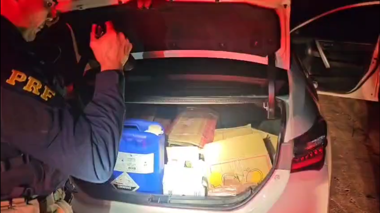 Imagem mostra policial clareando porta-malas de um carro. Nele, há 600 frascos de loló.