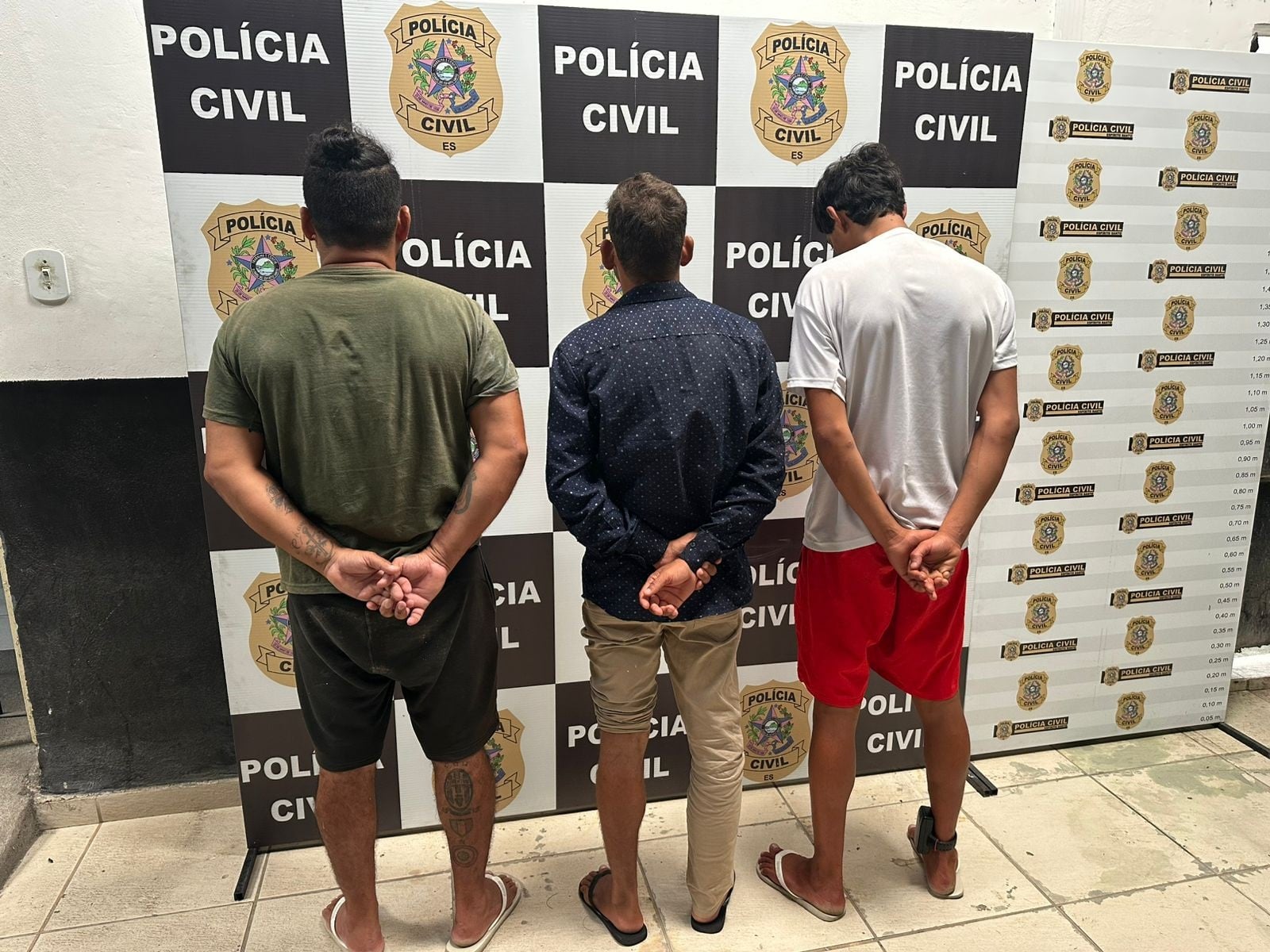 Imagem retrata três homens de costas após serem presos.