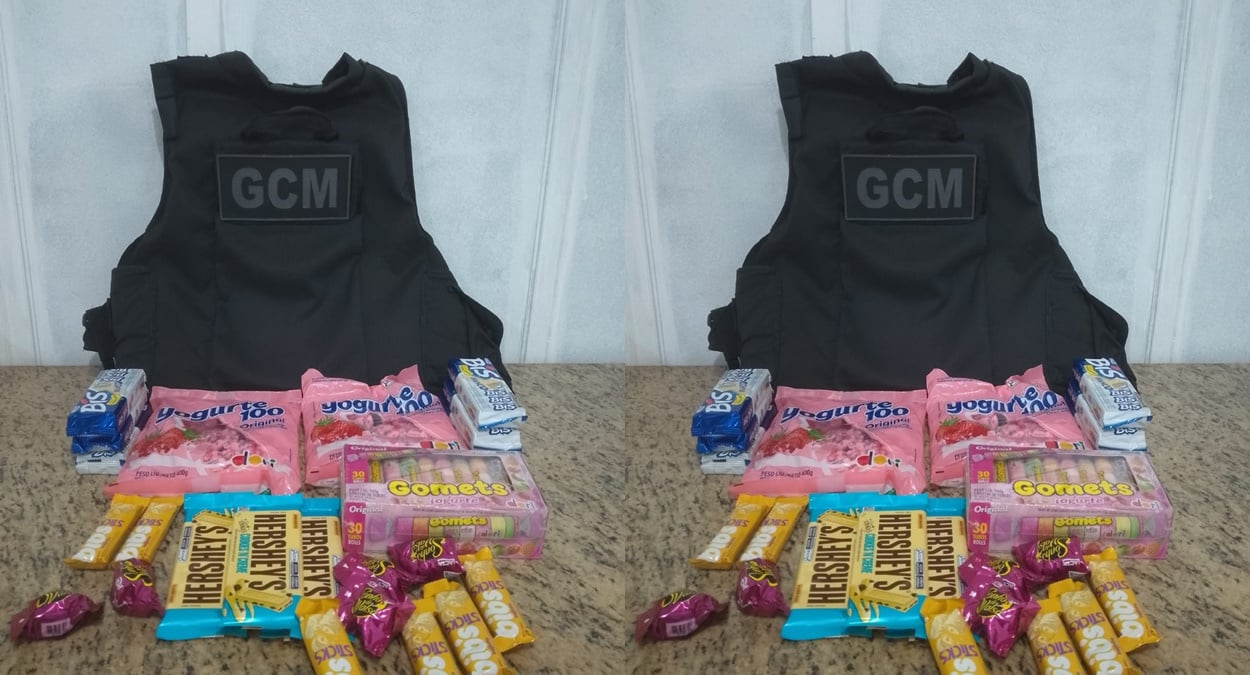 Produtos recuperados após furto de doces em Cachoeiro de Itapemirim, exibidos junto ao colete da Guarda Municipal, incluindo chocolates, balas e iogurtes.