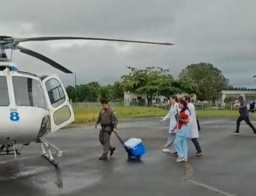 Equipe médica e militar caminha em direção a um helicóptero do NOTAER enquanto transporta uma caixa térmica azul usada no envio de órgãos para transplantes no Espírito Santo.