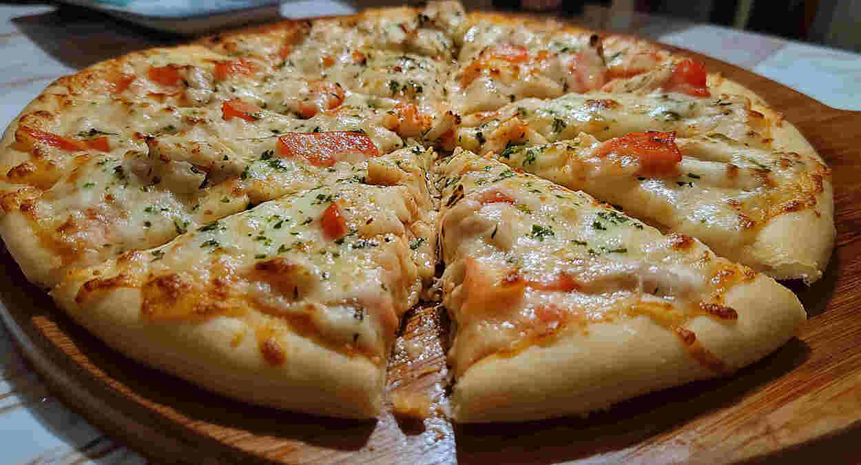 Pizza artesanal recém-assada em close, com borda macia e queijo derretido, representando o sabor caseiro oferecido pela Casa das Massas em Itaóca.